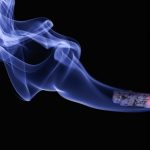 O imagine de prim plan a unei țigări aprinse și fum albastru care iese din ea.