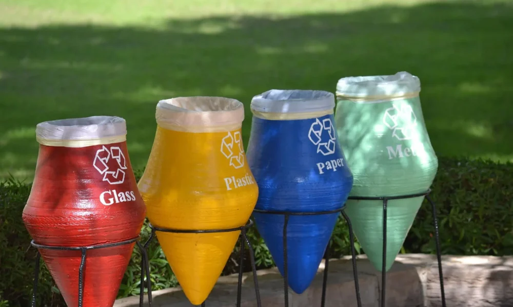 Cosuri colorate de reciclare pentru sticla, plastic, hartie si metal amplasate in aer liber, simbol al unui stil de viata sustenabil si al colectarii selective a deseurilor.