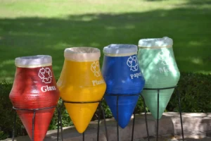 Cosuri colorate de reciclare pentru sticla, plastic, hartie si metal amplasate in aer liber, simbol al unui stil de viata sustenabil si al colectarii selective a deseurilor.
