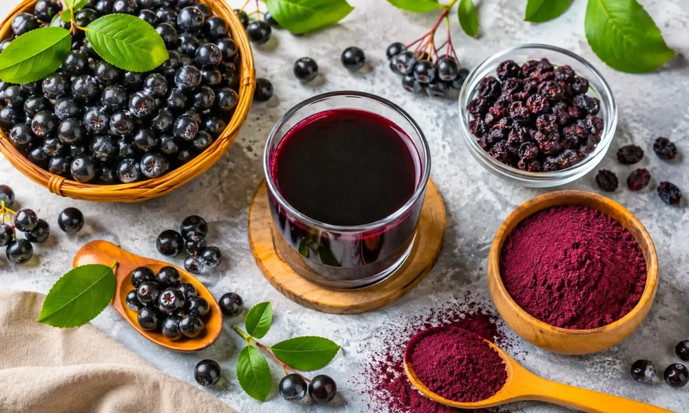 Aronia: beneficii, proprietăți, contraindicații și mod de consum Flat lay cu fructe proaspete de aronia, suc de aronia, fructe uscate și pudră de aronia, prezentând principalele forme de consum.